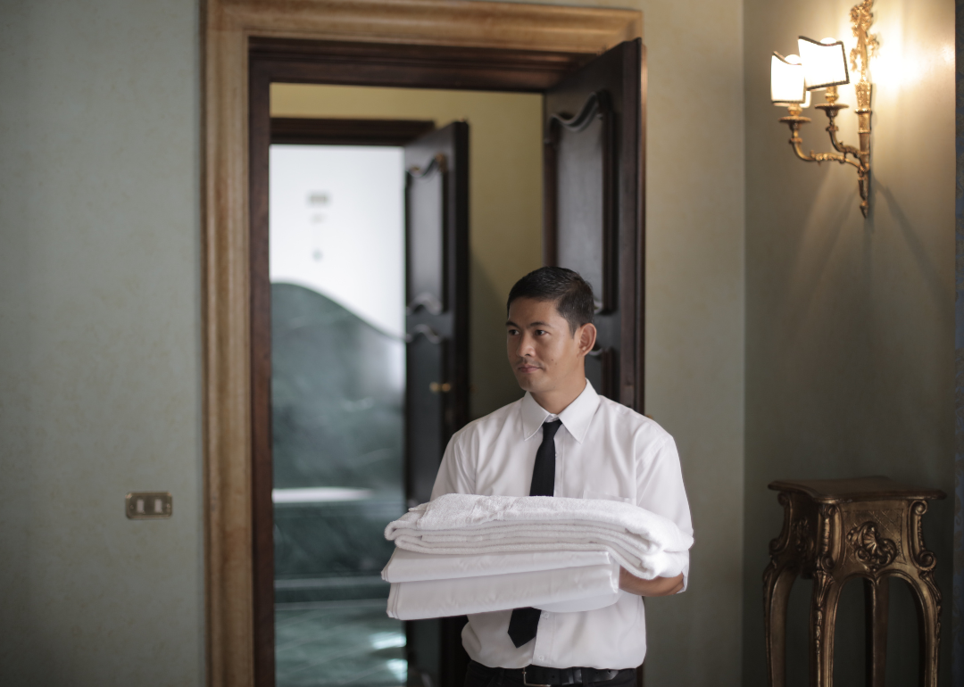 A member of a hotel's staff bringing fresh linens into a room.