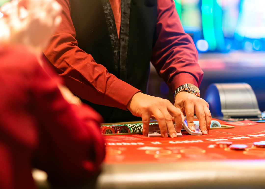 A croupier holding playing cards and gambling chips on table.