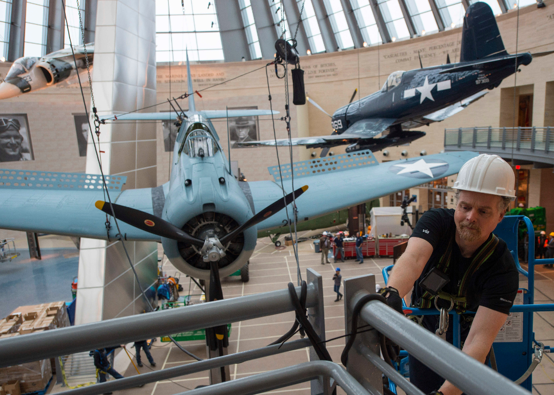 Lance Retallick, a technician with Weiss Theatrical Solutions, securing a safety line as a World War II SBD Dauntless dive bomber is craned into position at the National Museum of the Marine Corps in Triangle