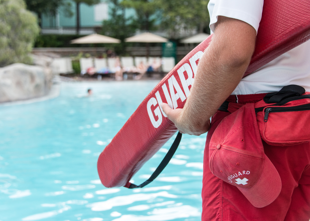 A lifeguard at a pool carries a flotation device.
