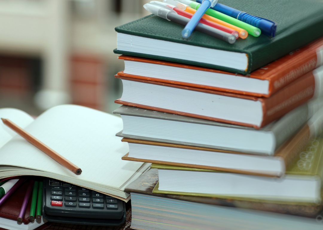 A stack of textbooks with pens on top of them next to an open notebook.