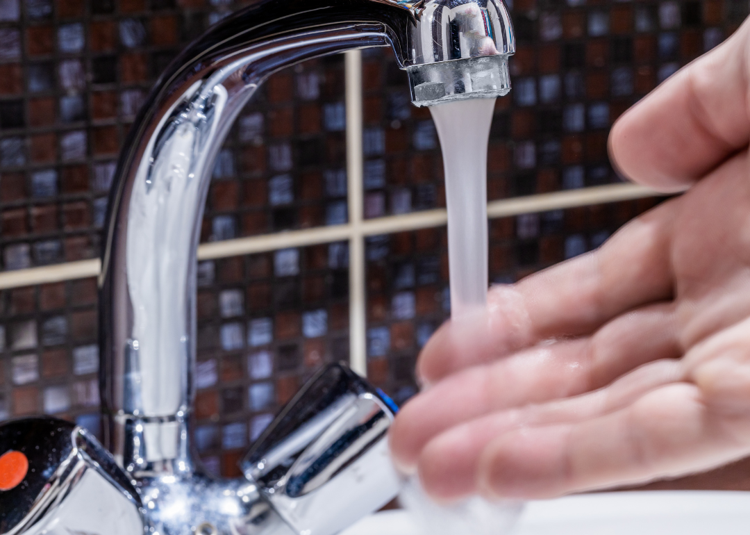 A person testing the temperature of water coming from a low-flow faucet using their hand.