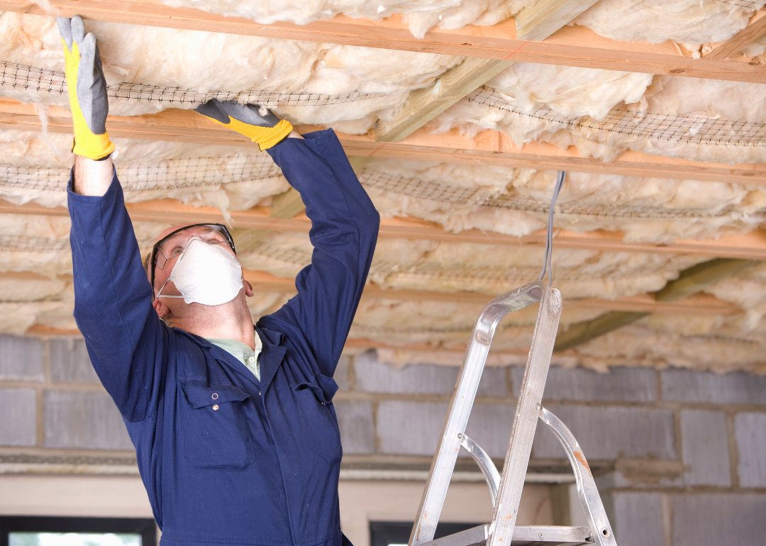 A worker in a protective mask and gloves who is installing ceiling insulation.