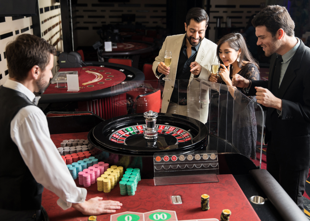 A gambling worker and players at a roulette wheel.
