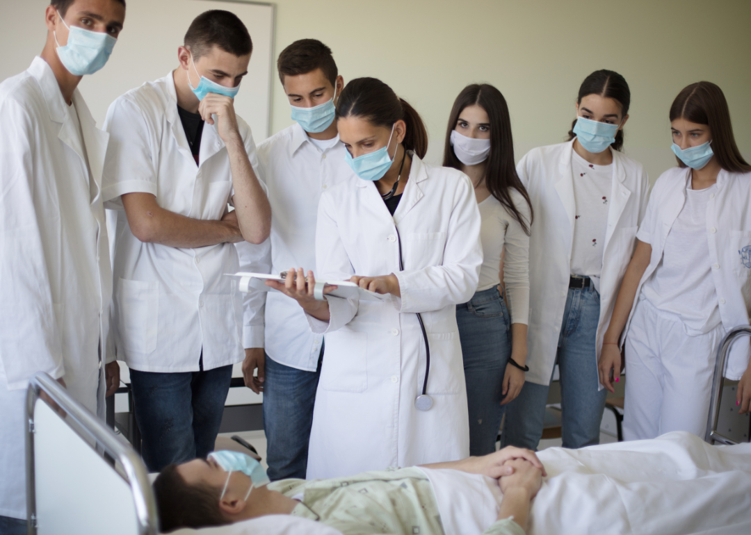 A nursing instructor with a group of nursing students in a hospital with a patient