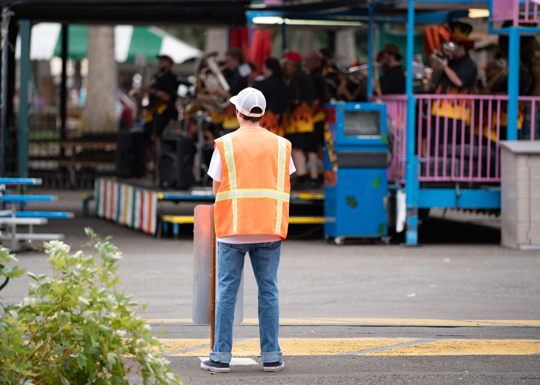 An amusement park worker stands with an orange vest.