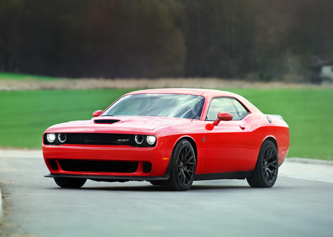 A red Dodge Challenger SRT Widebody standing on a secluded road by a field and forest.