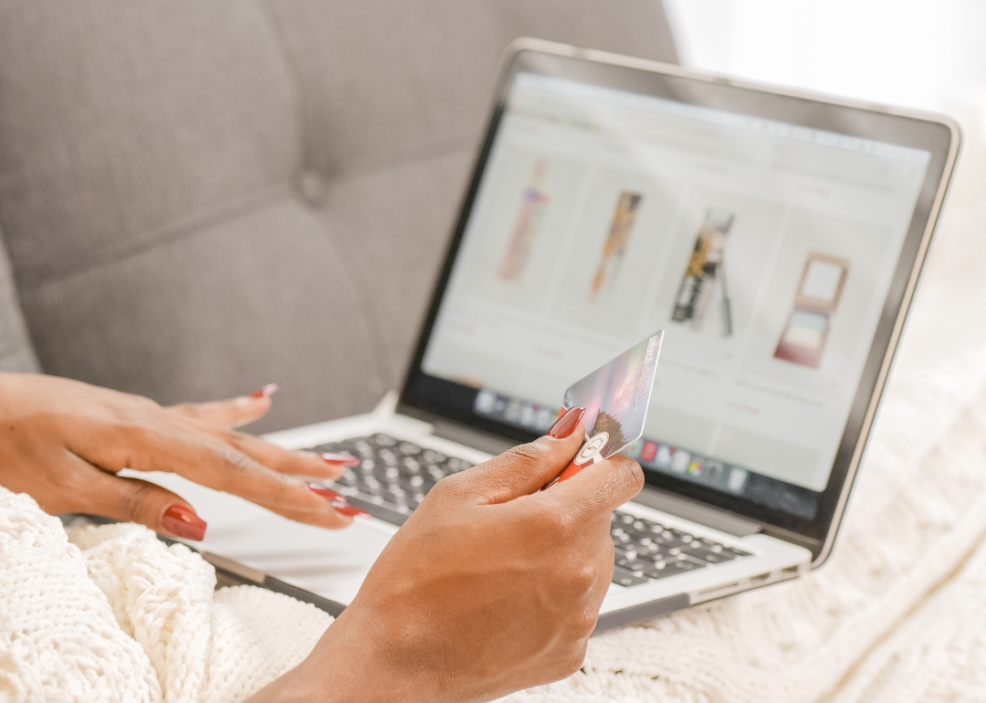 A person reclined on a couch while using their credit card to shop online.