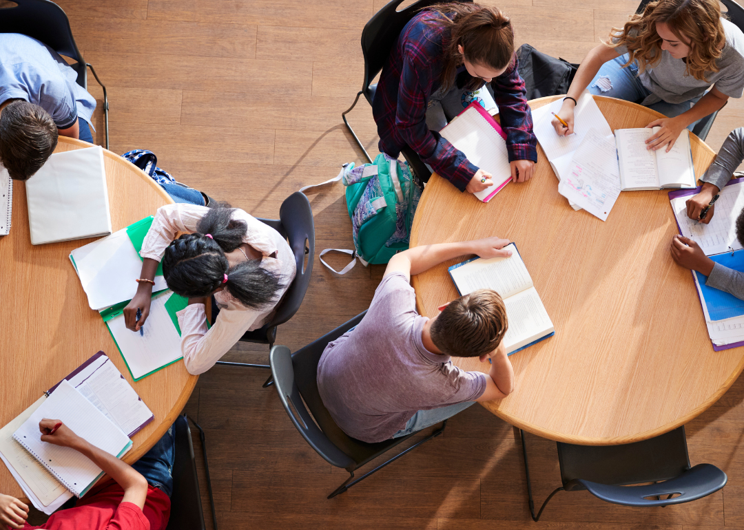 An overhead view of high school pupils in group study sitting around circular tables.