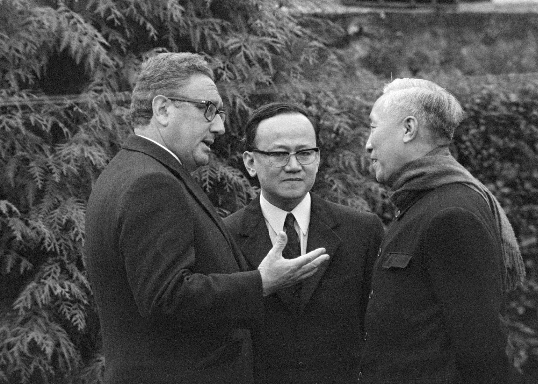 An interpreter standing between White House Advisor Henry Kissinger and Le Duc Tho.