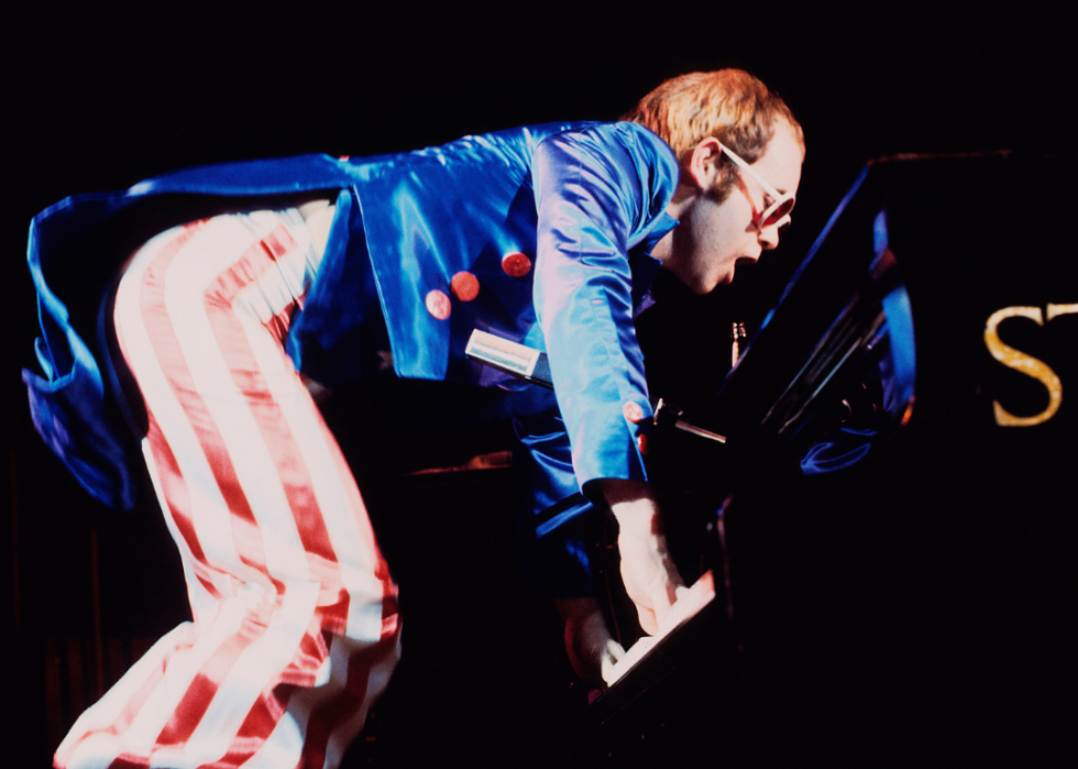 Elton John performs onstage in a red, white and blue satin outfit.