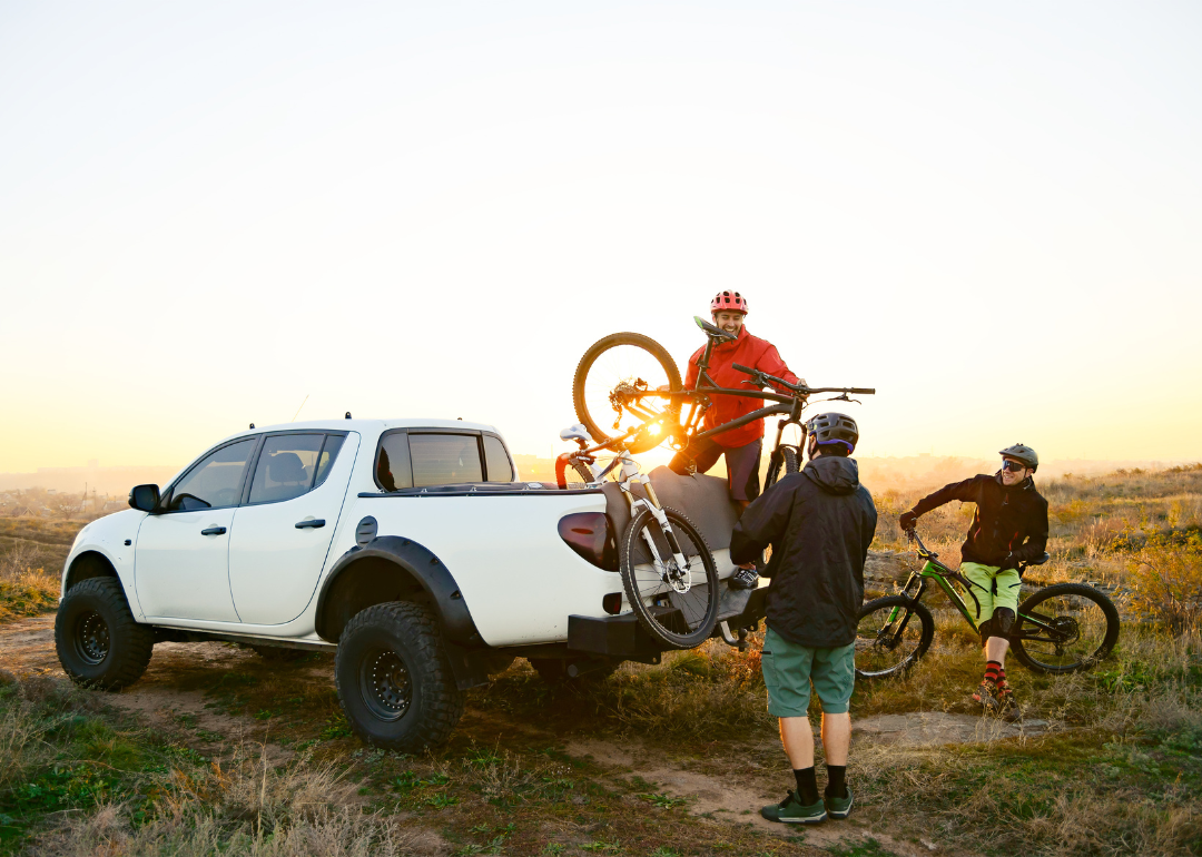Cyclists taking their bikes out of the bed of a pickup truck.
