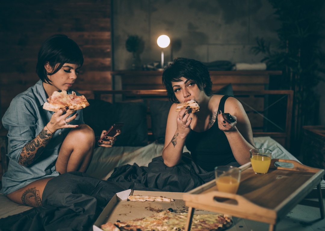 Two people eating a large meal of pizza in bed before going to sleep