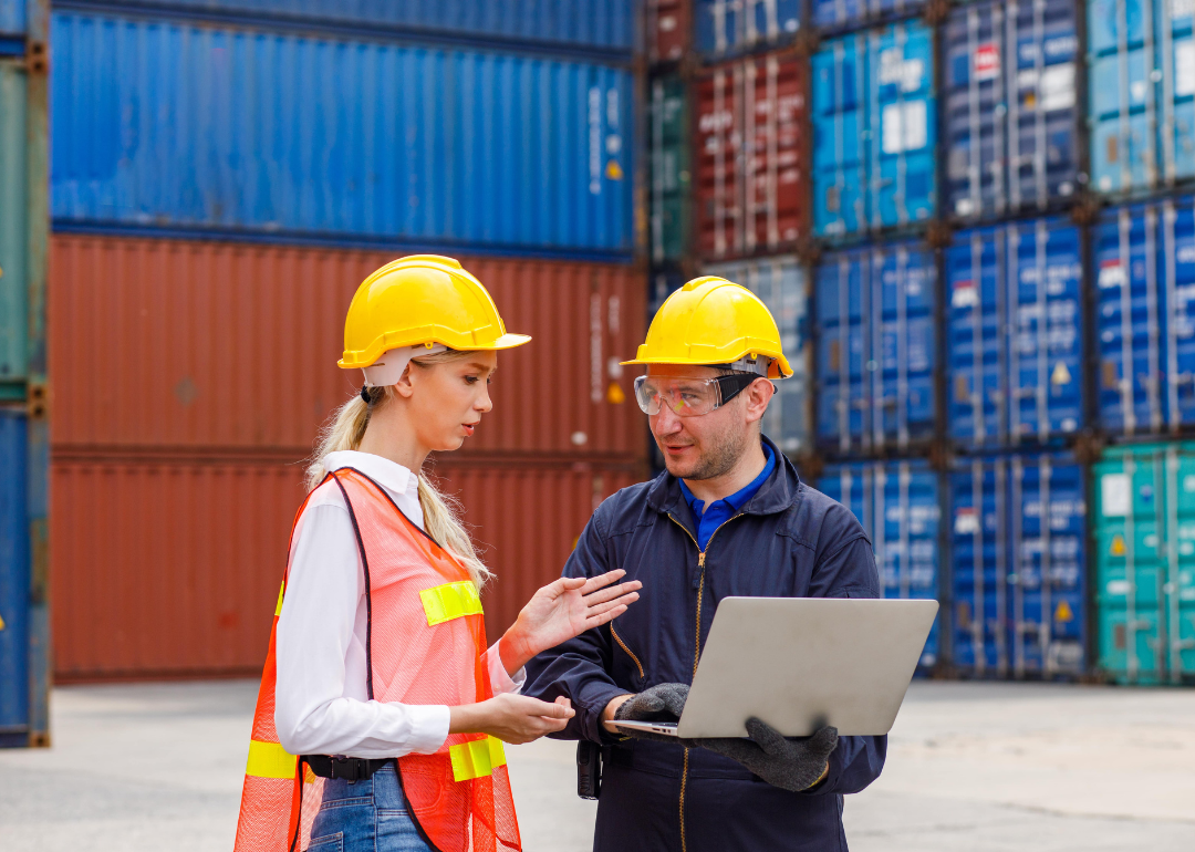 Two logisticians discuss supply chain issues at a shipping container yard