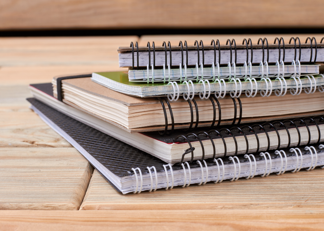 A stack of spiral noteboooks in front of a wooden background.