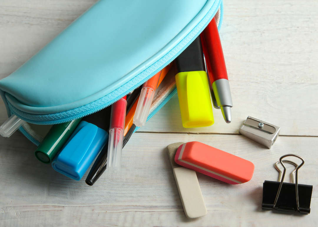 A pencil case full of pens, pencils, and highlighters spilling on a table.