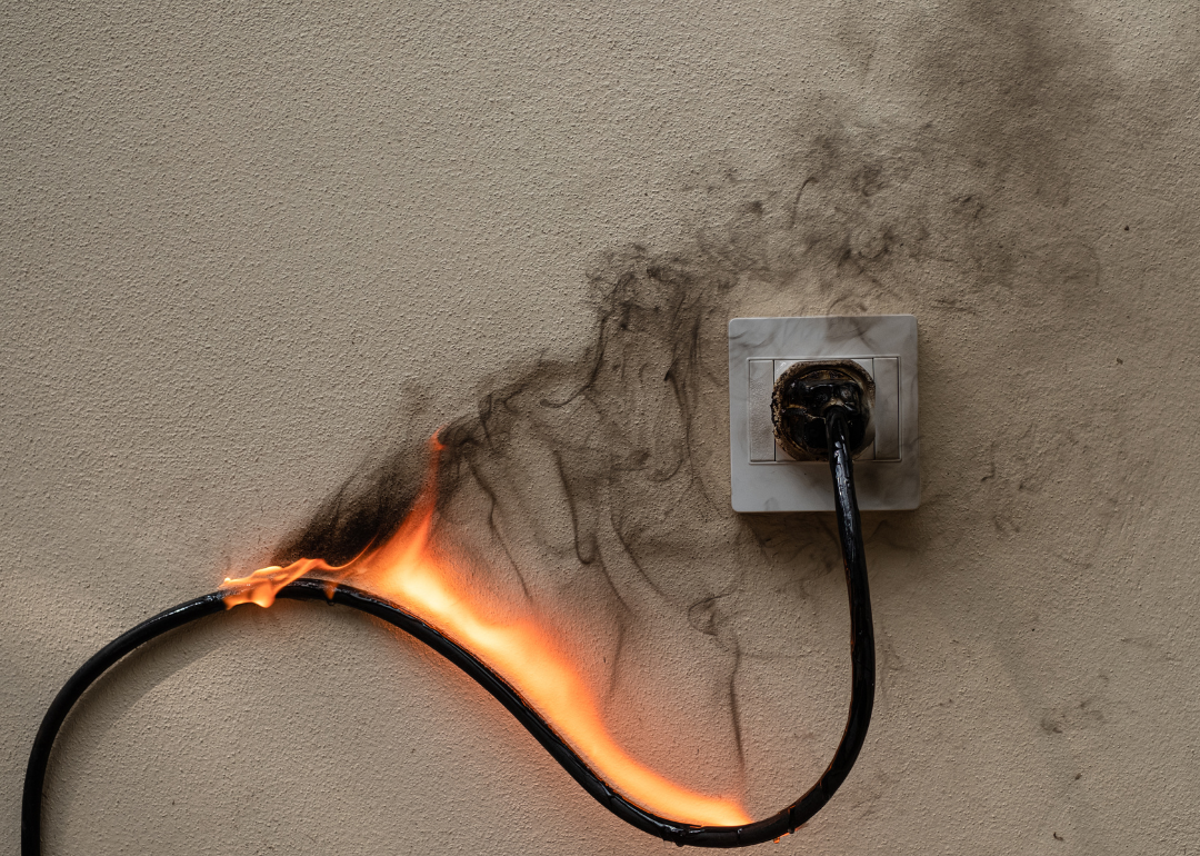 An outlet with an on-fire cord connected to it.
