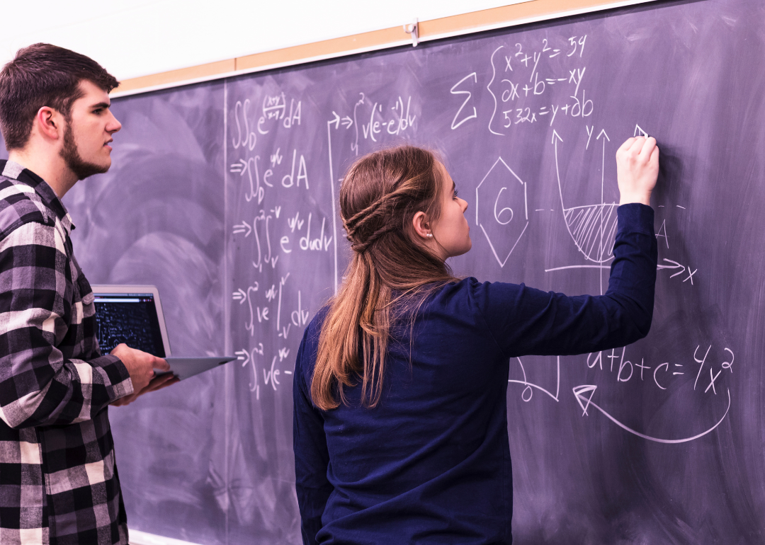Students solving a calculus problem on a blackboard.