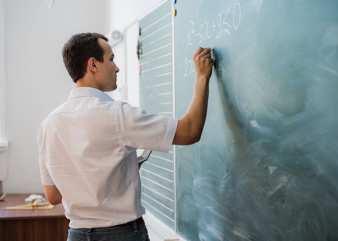 A teacher writing an equation on a blackboard using chalk.