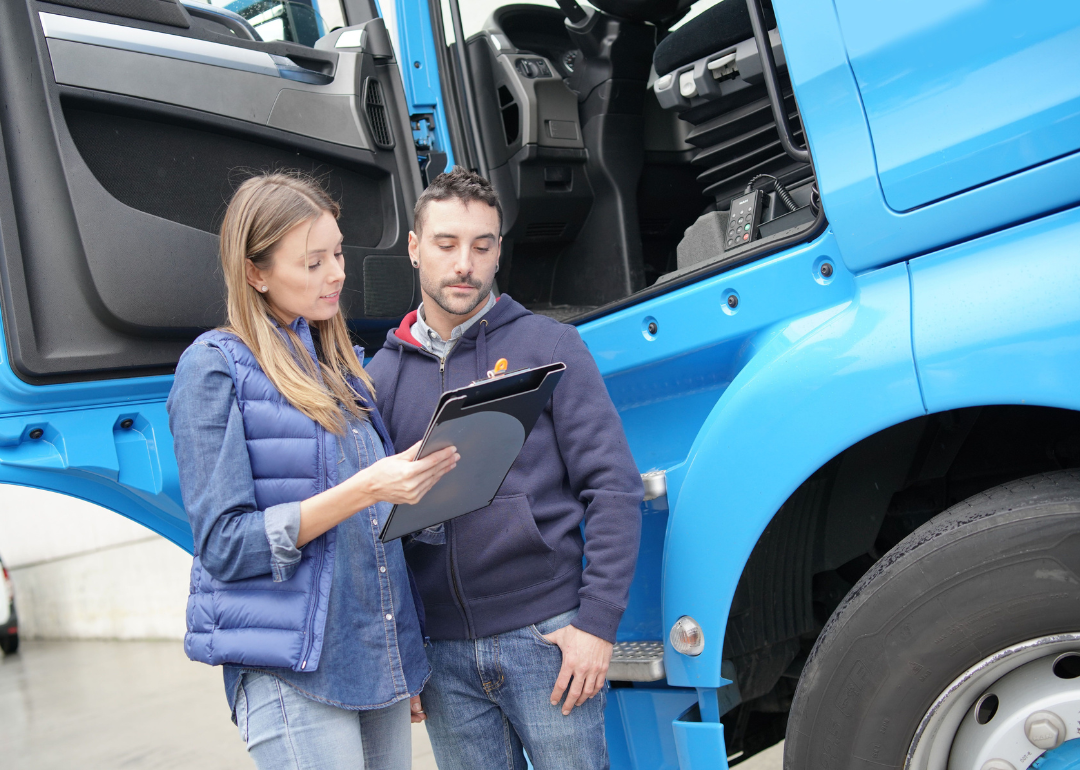 Woman going over information on a clipboard to man in front of a blue truck.