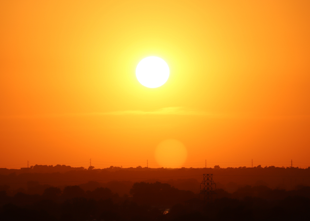 The sun setting on a blistering hot summer day over the power lines and tress of Lincoln.