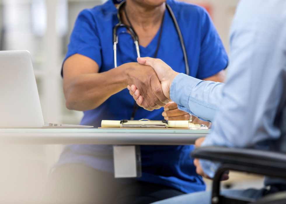 Doctor and patient shake hands, seated at a table.