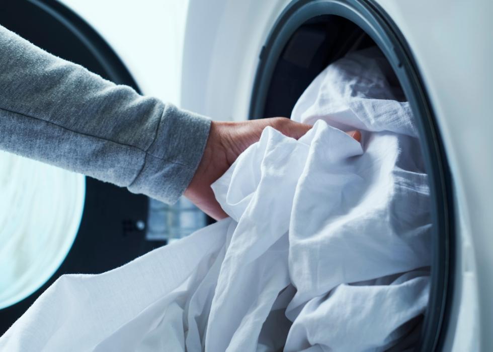 A person placing bedding items into a washing machine.