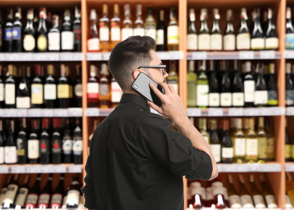 An employees speaks on the phone in front of shelves of wine in a wholesale outlet. 