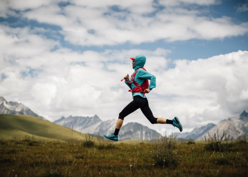 A woman running energetically across a scenic outdoor landscape.