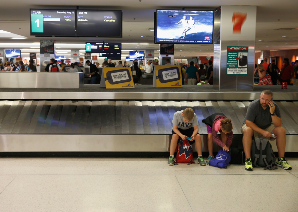 A man and two children sitting on the edge of an empty luggage carousel.  