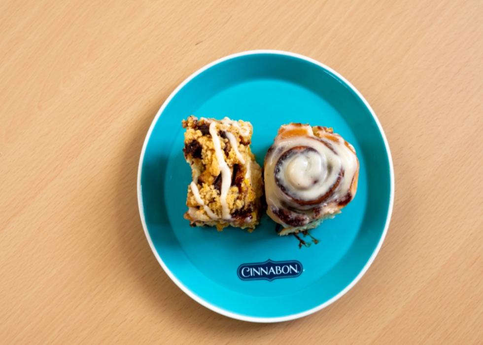 Cinnabon treats, a coffee cake and a cinnamon roll, on a blue plate.