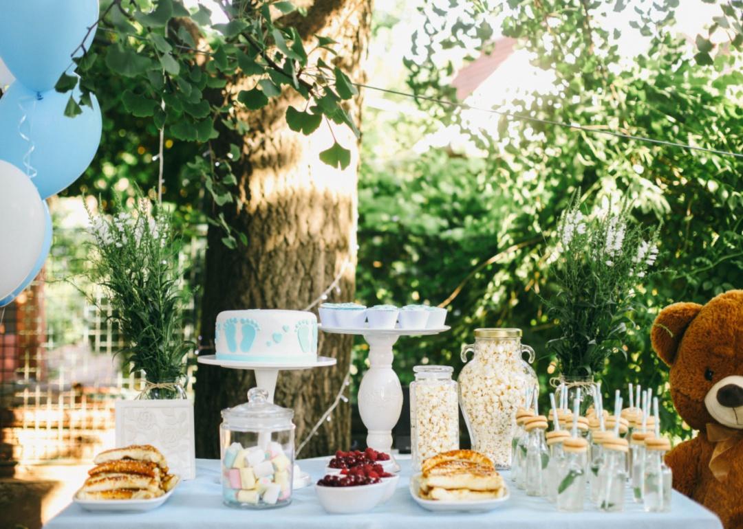 Blue balloons and decorations for a baby shower set up at a table in a backyard.