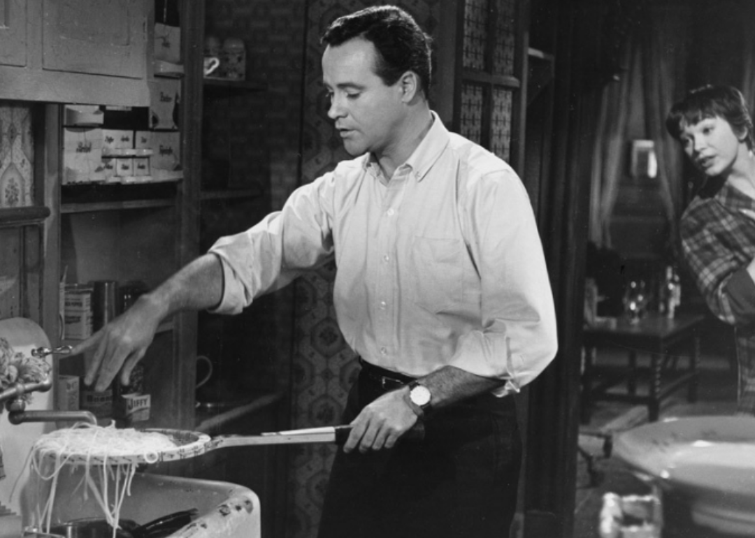 Jack Lemmon draining pasta with a tennis racket while Shirley MacLaine looks on.