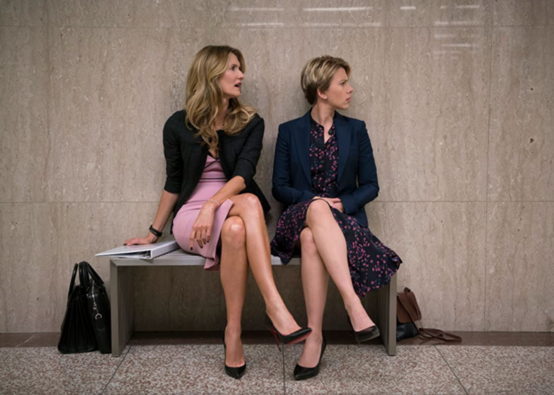 Scarlett Johansson and Laura Dern sitting on a bench looking to the side.