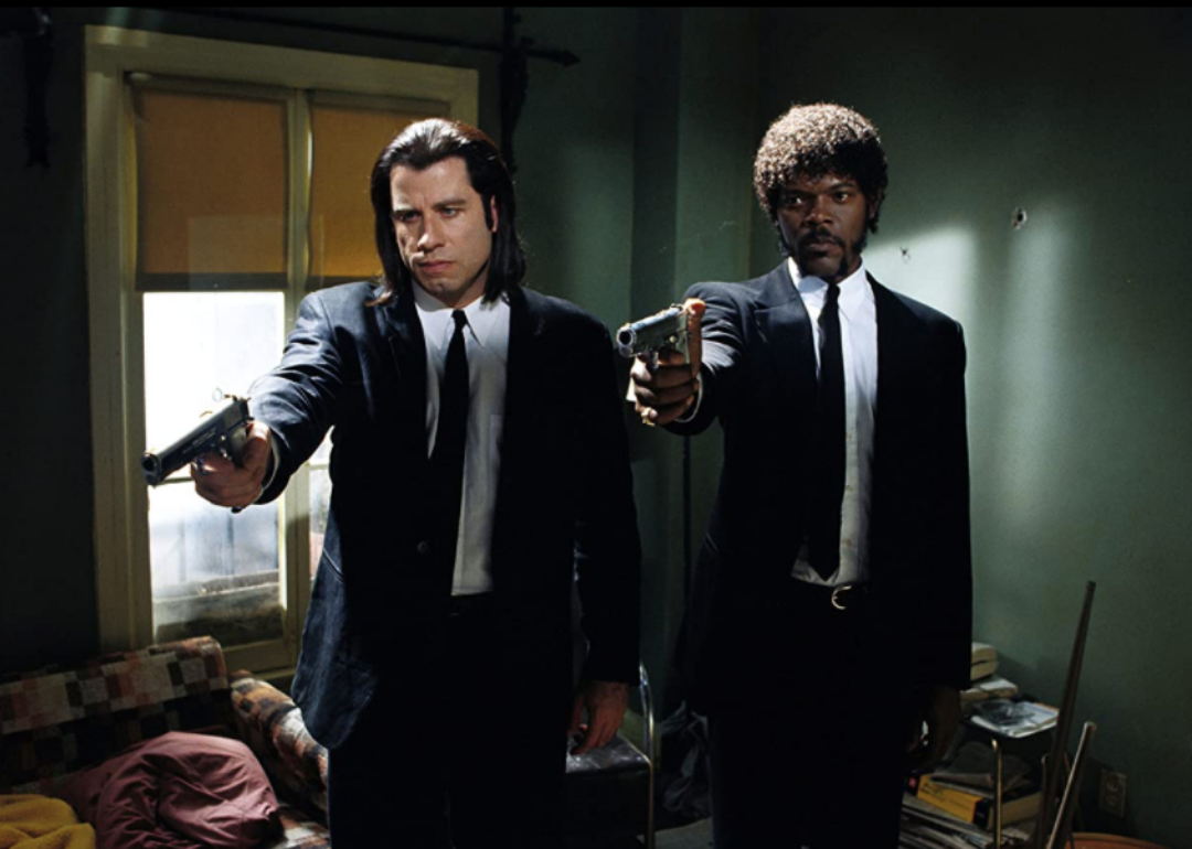 John Travolta and Samuel L. Jackson in black suits pointing guns.