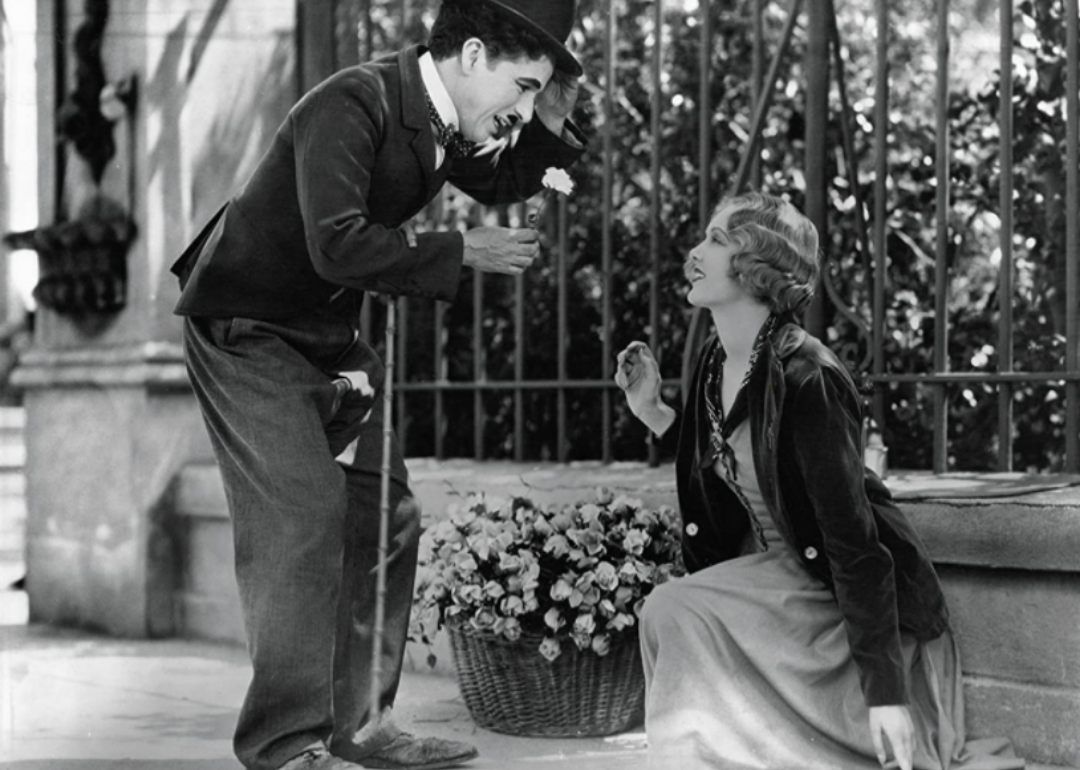 Charles Chaplin holding a flower for a woman kneeling down.