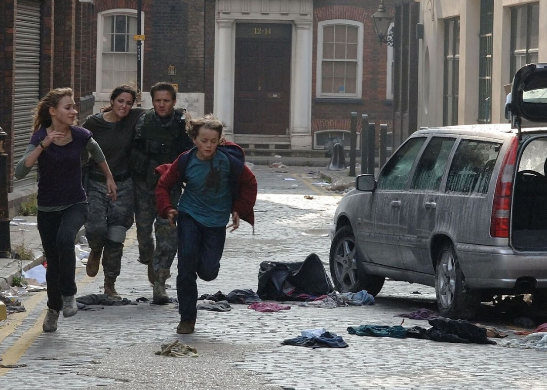 A man, woman and young boy and girl running through a disaster scene in a city.