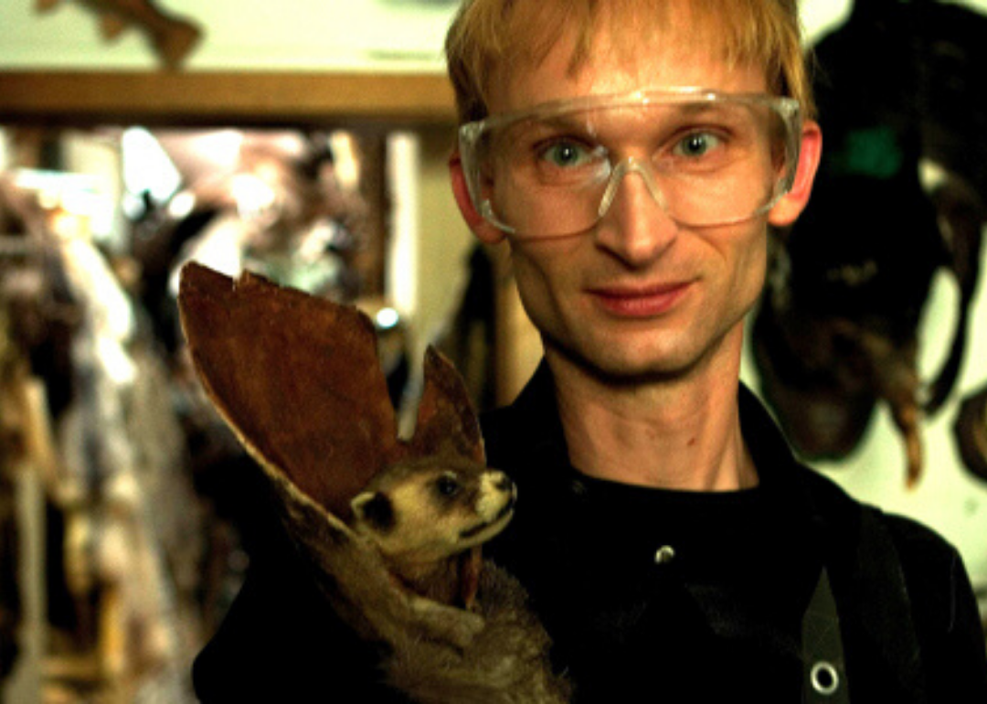 A man in clear goggles holding a small taxidermied animal.