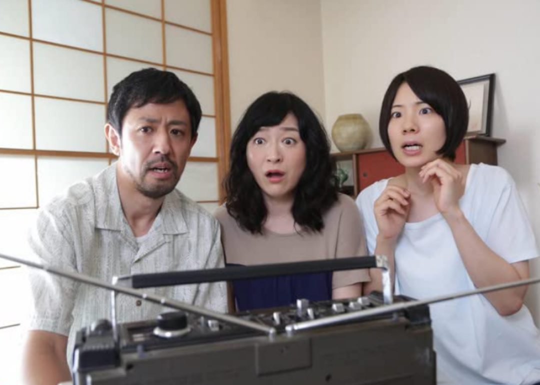 A man and two women look surprised as they listen to a radio with an large antennae.