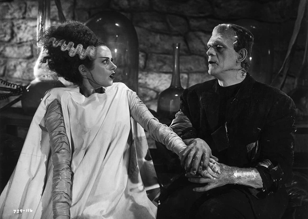 Frankenstein stares at his man-made monster bride, who has black hair with a silver lightening strike on the side.