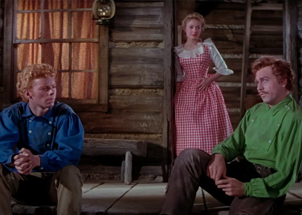 Three people sitting on a log cabin porch.