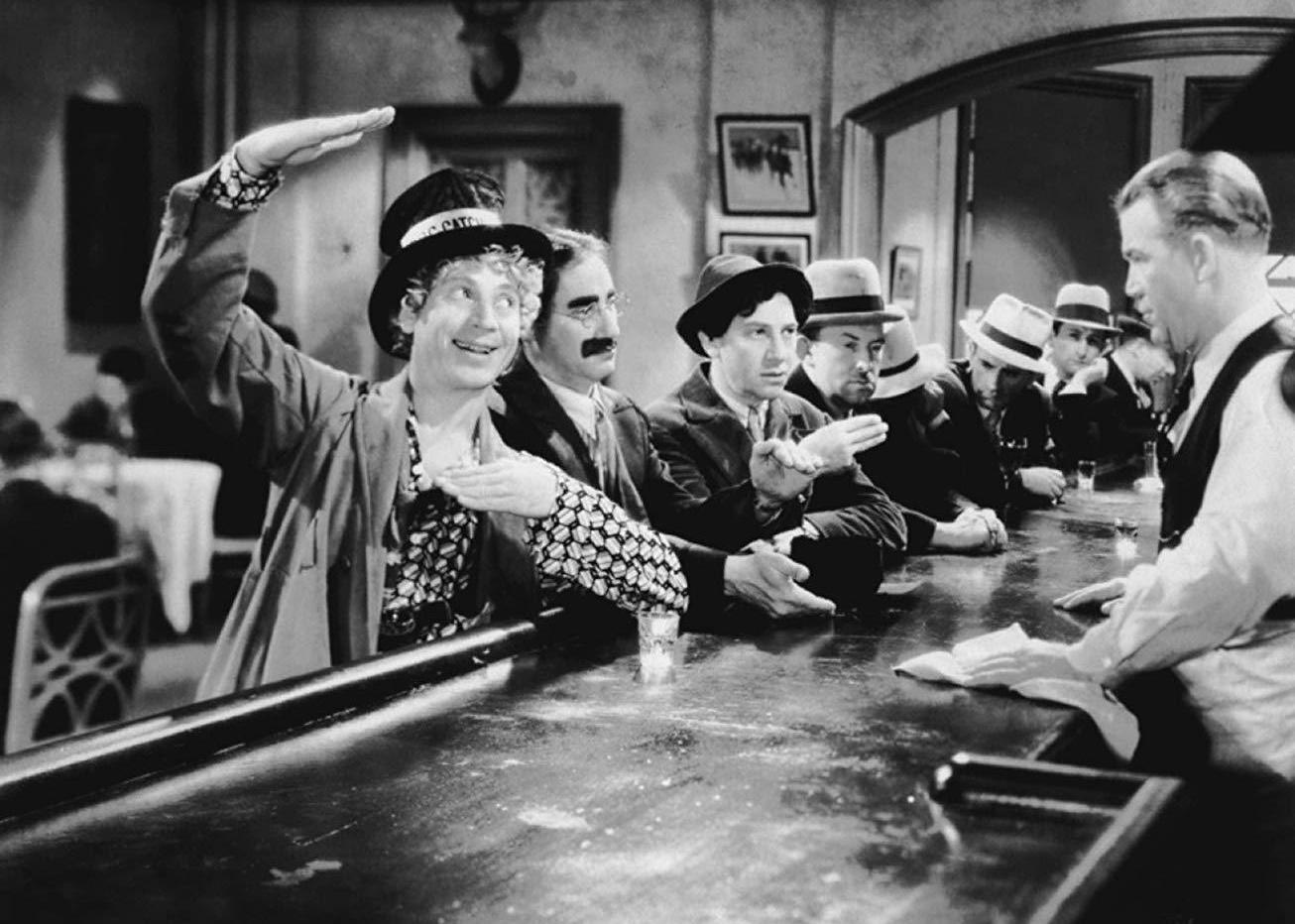 The Marx Brothers sitting at a bar talking to a bartender.