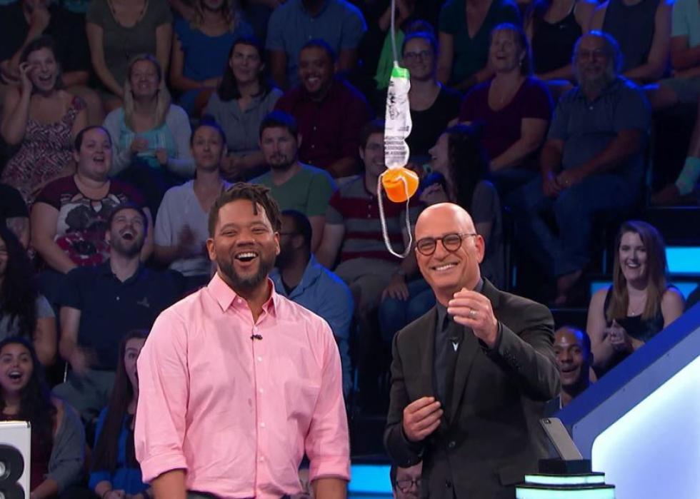 Howie Mandel and his guest on the show laughing at an oxygen mask hanging in front of them.