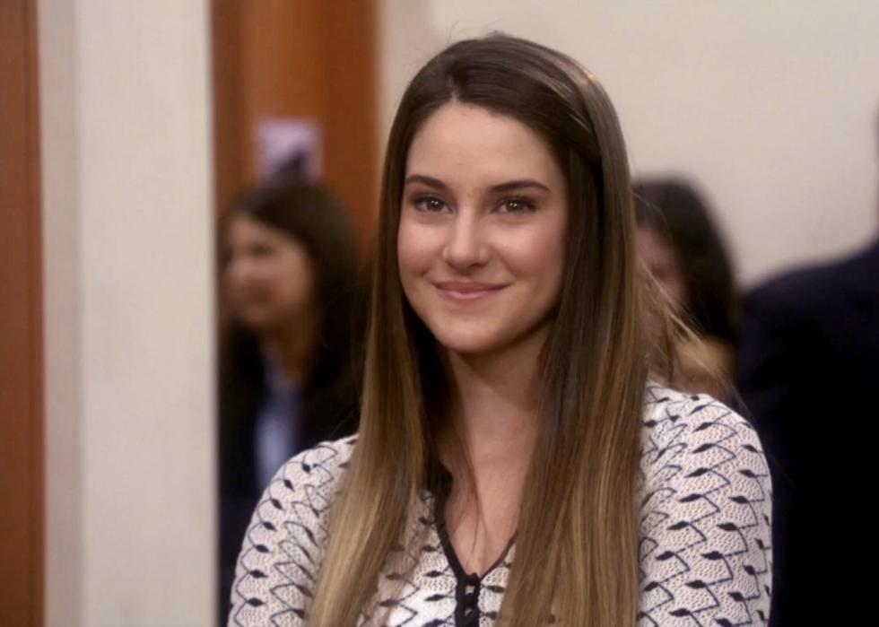 A girl with long brown hair smiles in a school hallway.