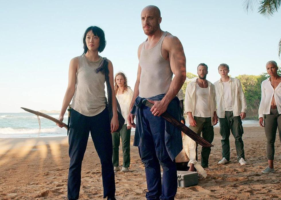 A group of people all wearing white shirts on the beach stare at something in anger.