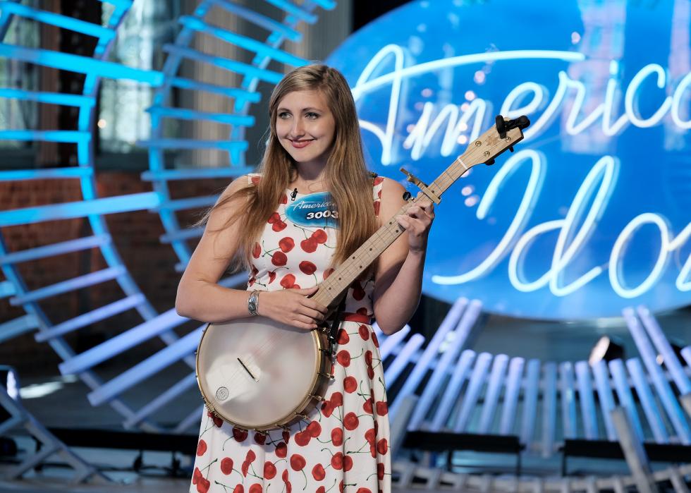 Girl plays an instrument in front of the American Idol sign onstage.