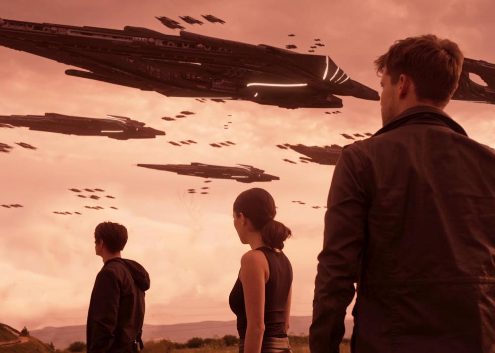 Three young people stand looking at a spaceship in the sky.