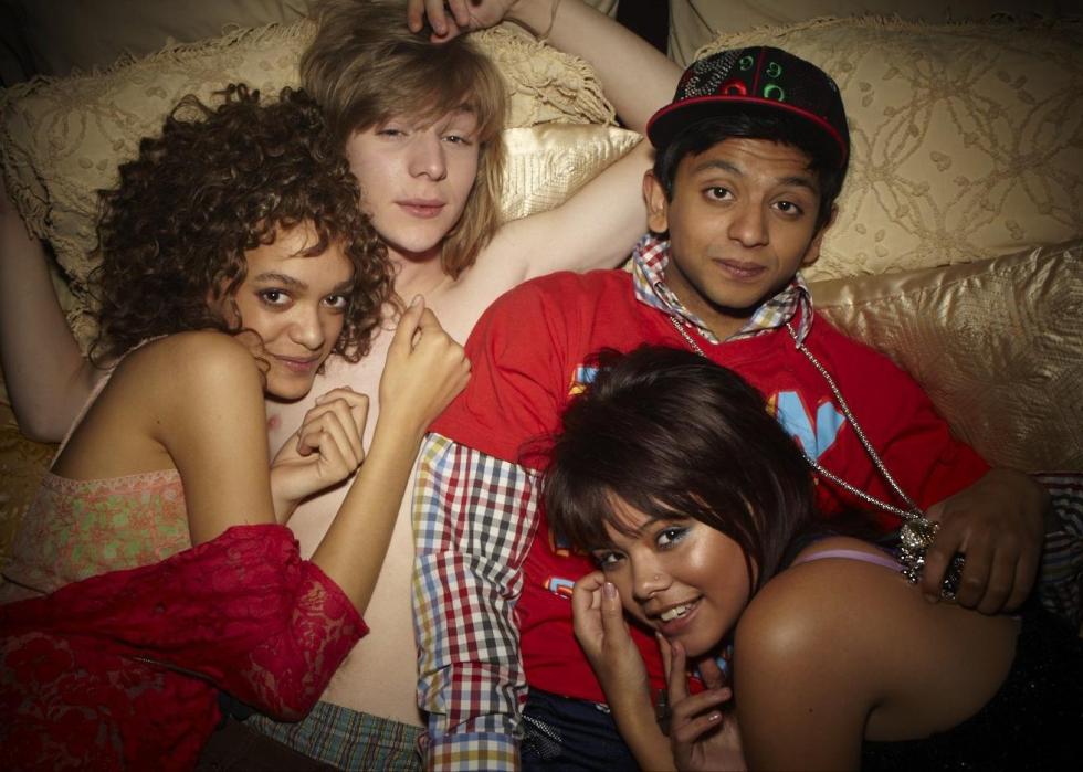 A group of teens lay on a bed snuggled together.