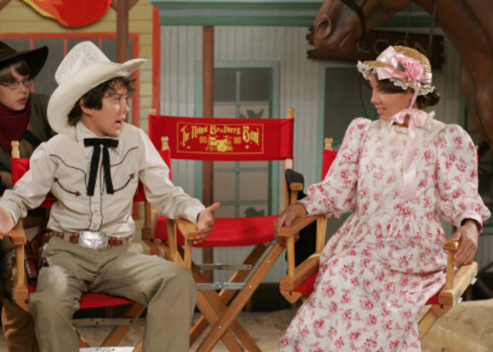 A boy and girl dressed up in a western theme sitting in chairs.