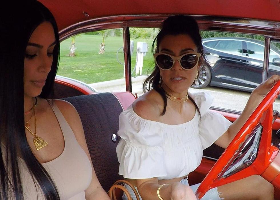 Kim and Kourtney Kardashian riding in a red classic car.